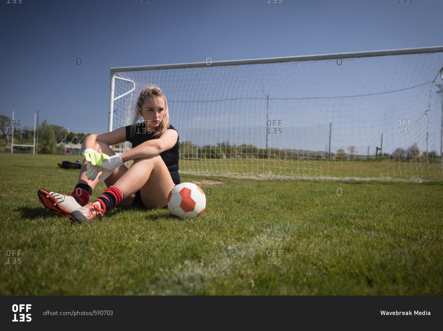 Full length of female soccer player relaxing by goal post on playing field