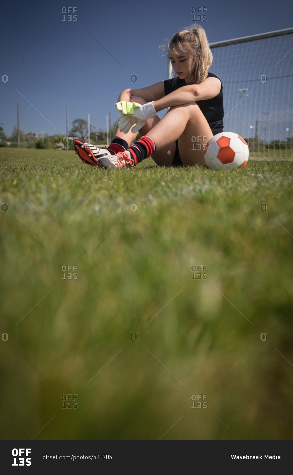 Full length of tired female soccer player sitting by goal post on field