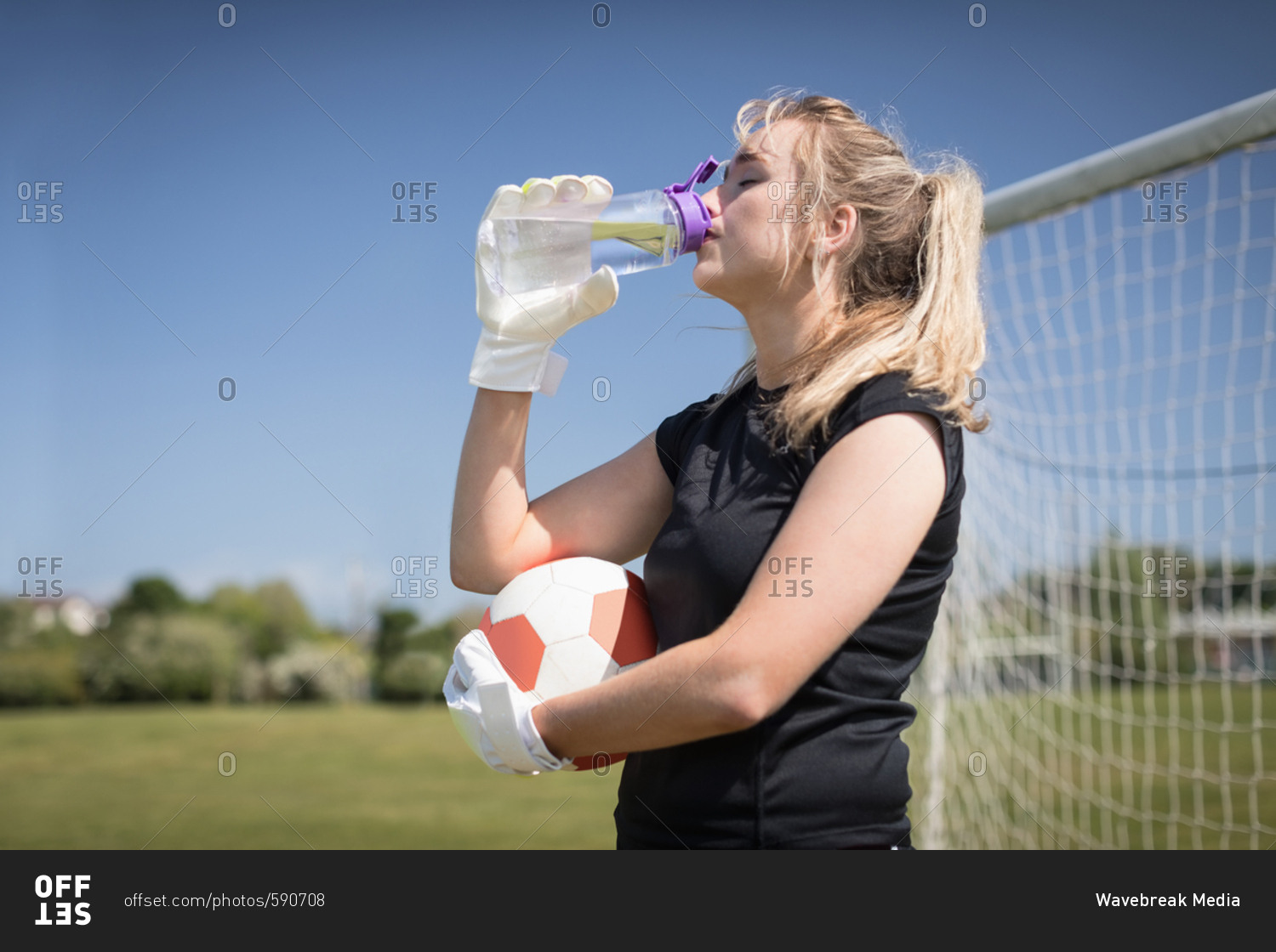 Thirsty female soccer player drinking water on field during sunny day