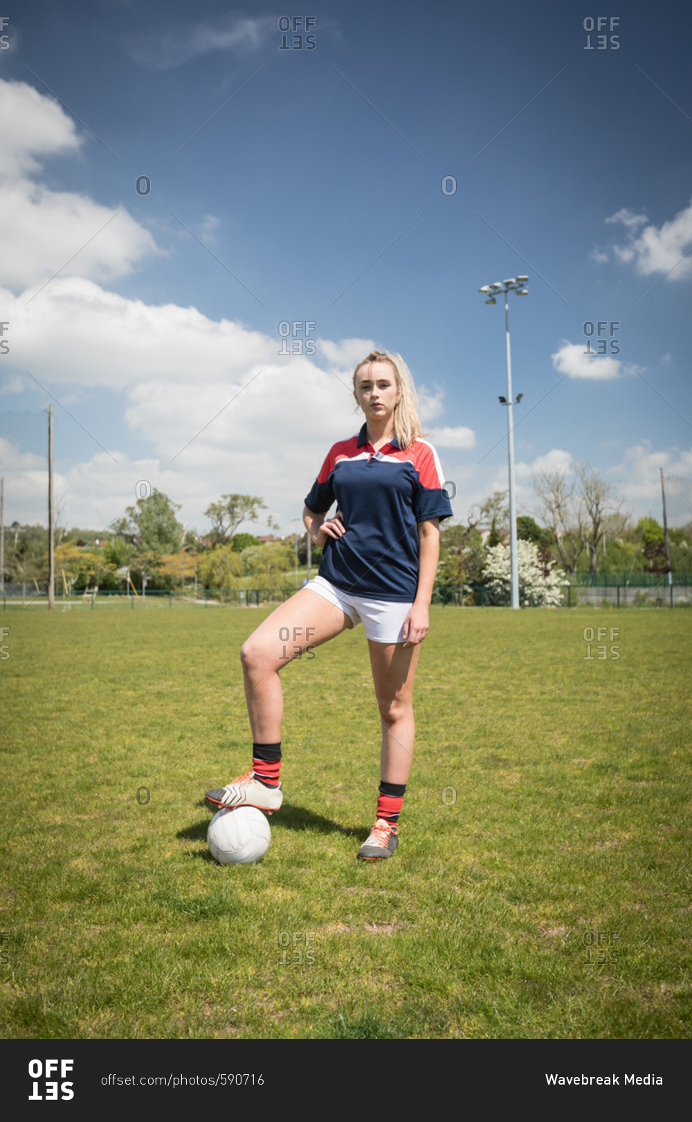 Full length of female soccer player with ball standing on field against sky