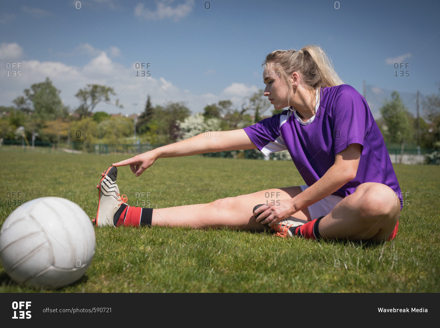 Full length of female soccer player by ball stretching on field