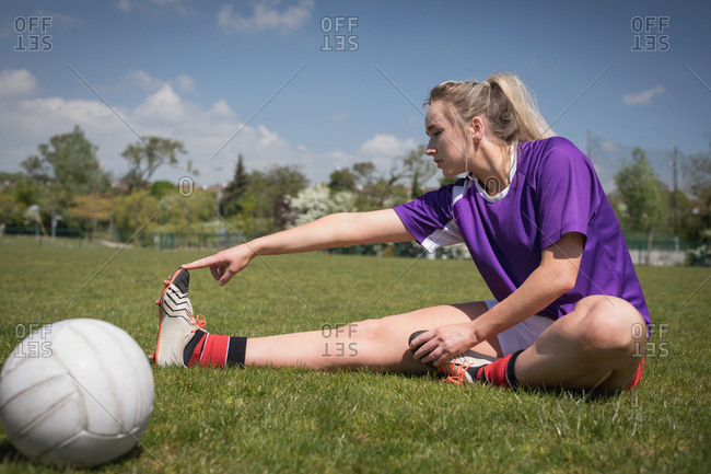 Full length of female soccer player by ball stretching on field | Stock ...