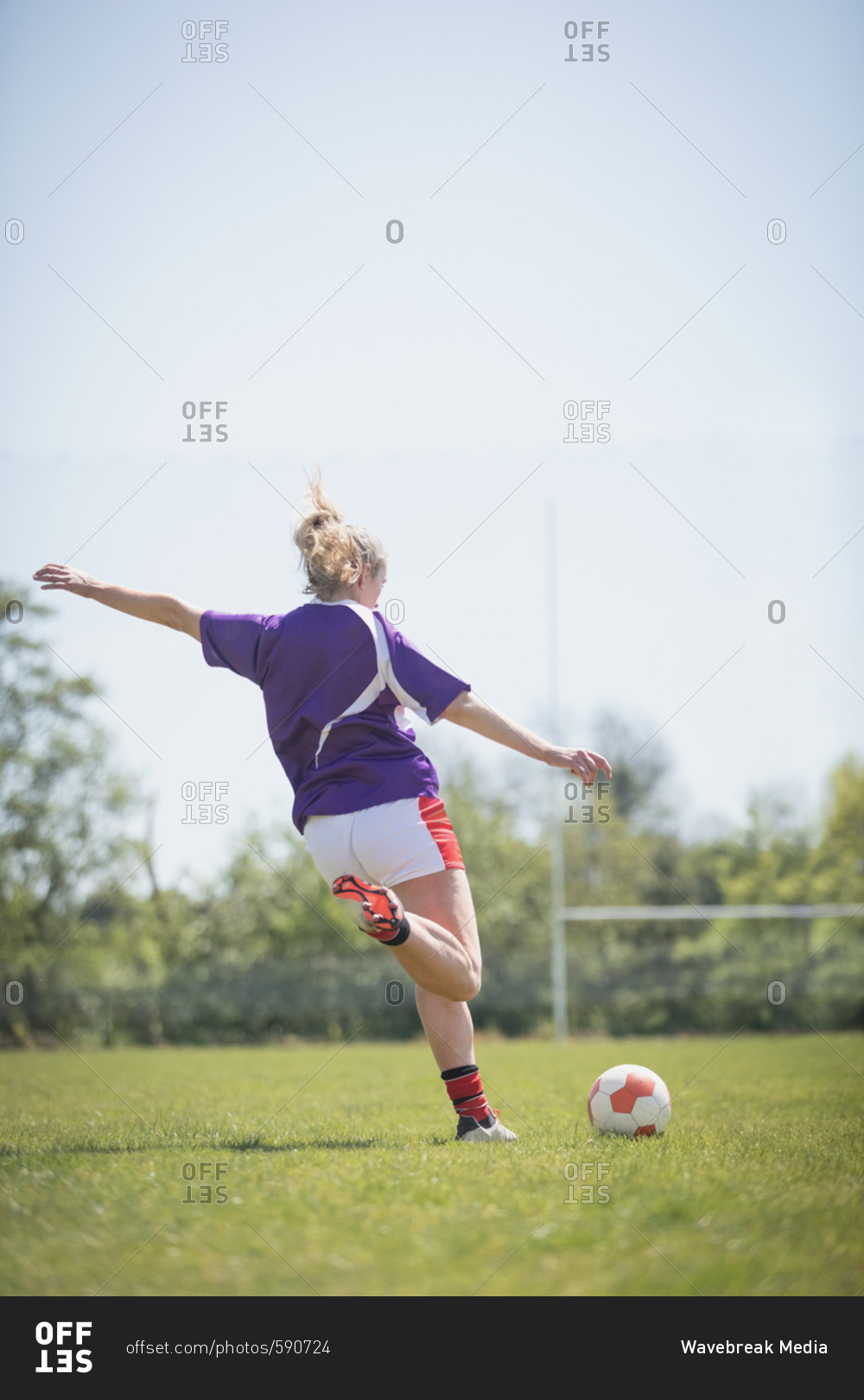 Rear view of woman kicking soccer ball on field against clear sky