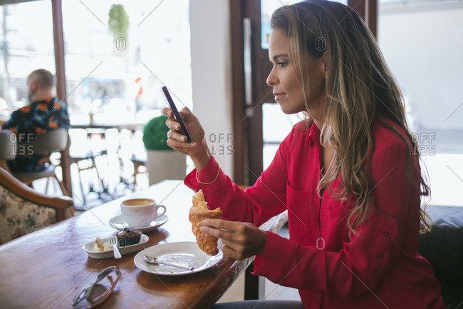 Woman holding croissant using phone