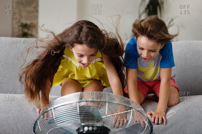 Two kids on couch playing with fan