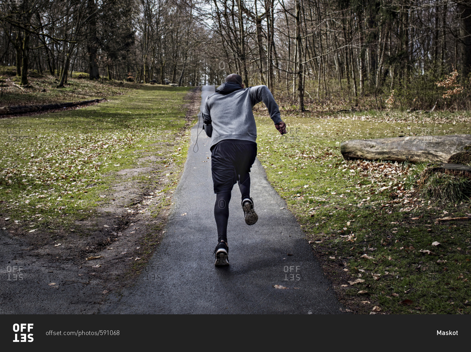 Full length rear view of determined male athlete jogging on narrow street in forest