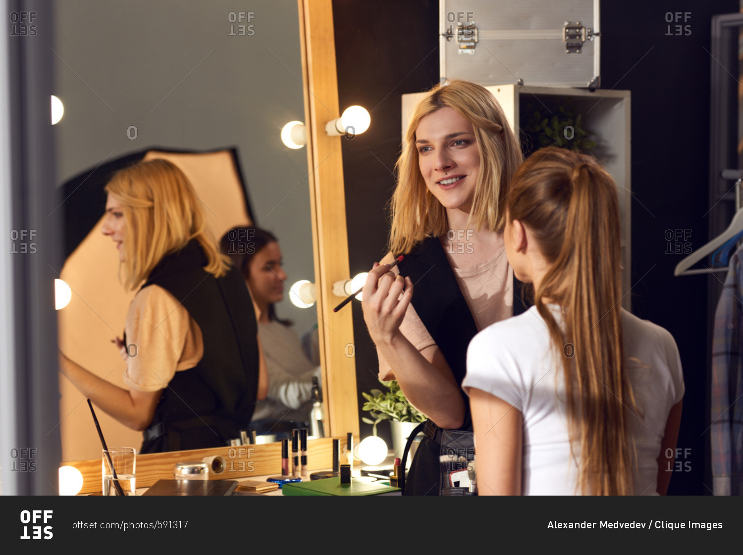 Transwoman in love with her profession. Young transgender make-up artist working with female model in studio and smiling cheerfully