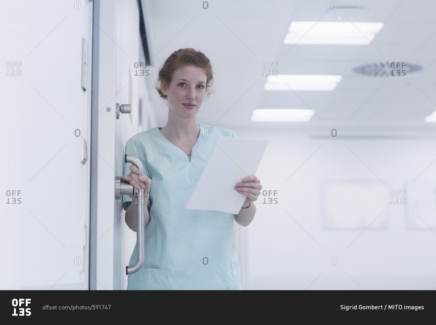 Portrait of nurse holding  handle of door and medical charts