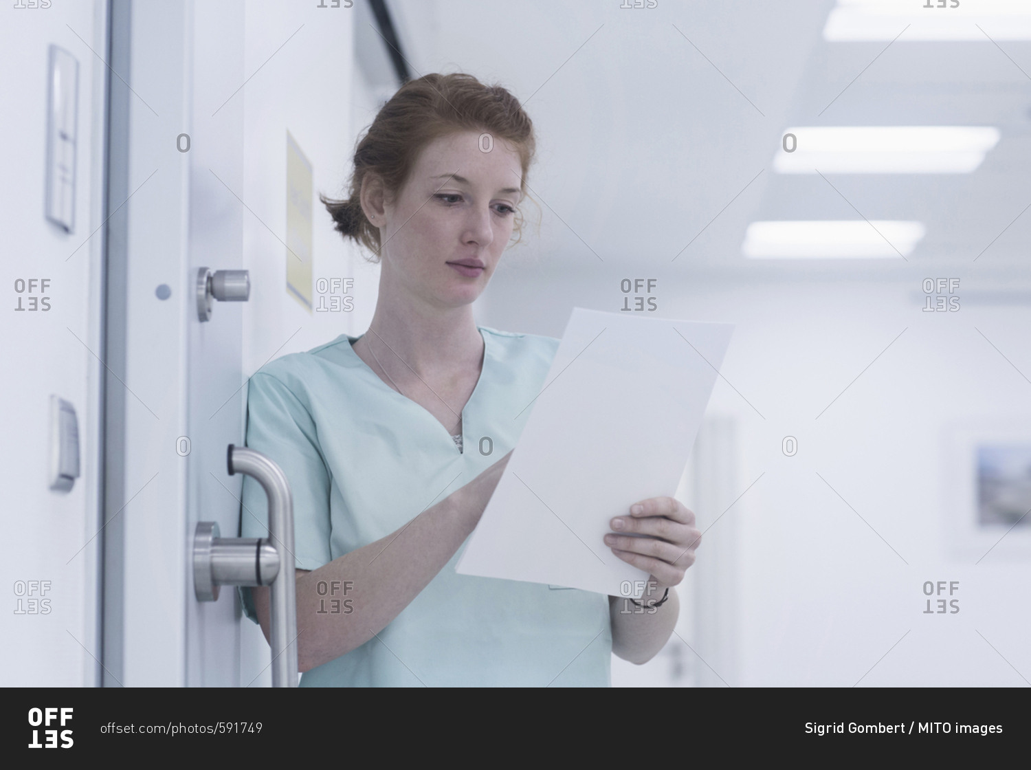 Young nurse reading medical charts while leaning  by door
