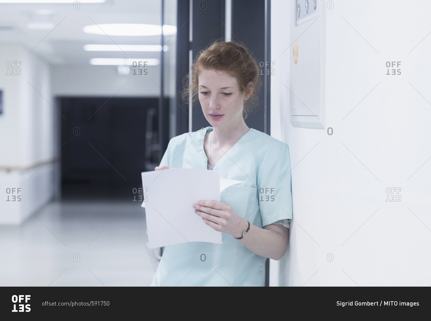 Young nurse reading medical charts while leaning by door