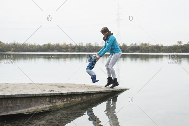 Mother and son jumping hand in hand on a landing stage at a lake in the autumn