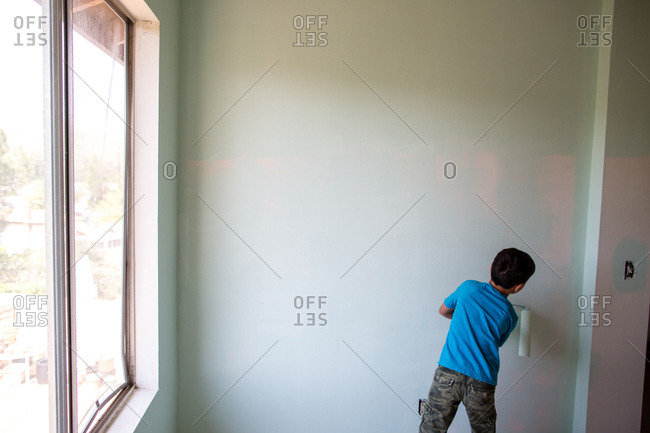 Rear View Of Boy Painting Wall With Paint Roller At Home