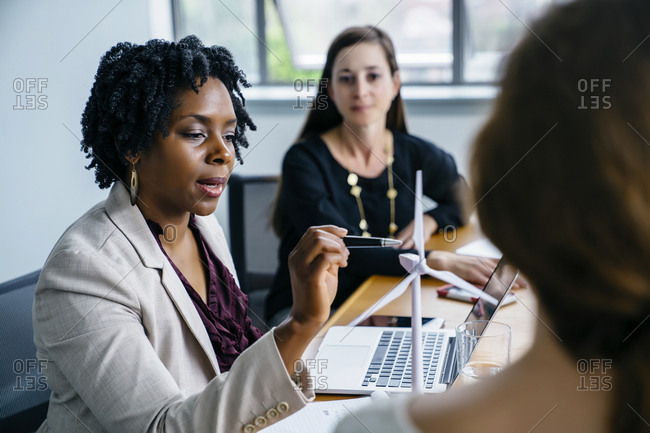Businesswoman explaining wind turbine model to female colleagues in office