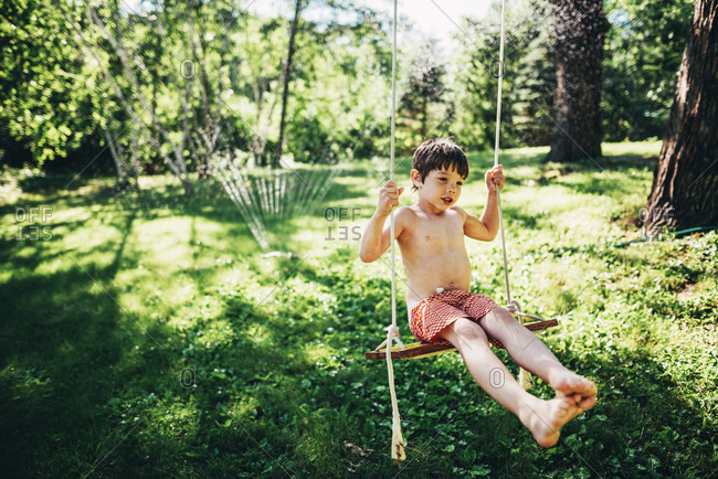 Young boy on backyard swing playing in a sprinkler