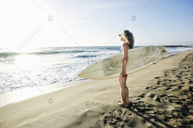 Older Caucasian woman standing on beach holding surfboard