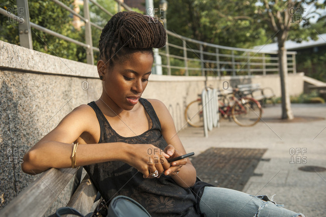 African American woman on bench at park texting on cell phone