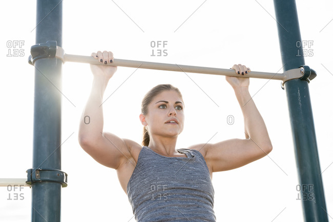 Hispanic woman doing chin-up outdoors