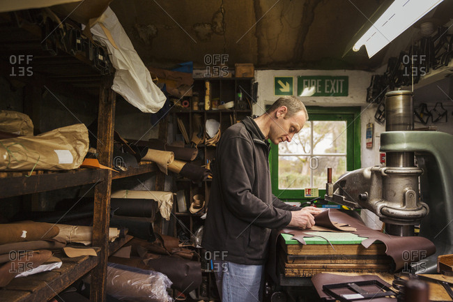 Man standing in a shoemaker's workshop, cutting brown leather