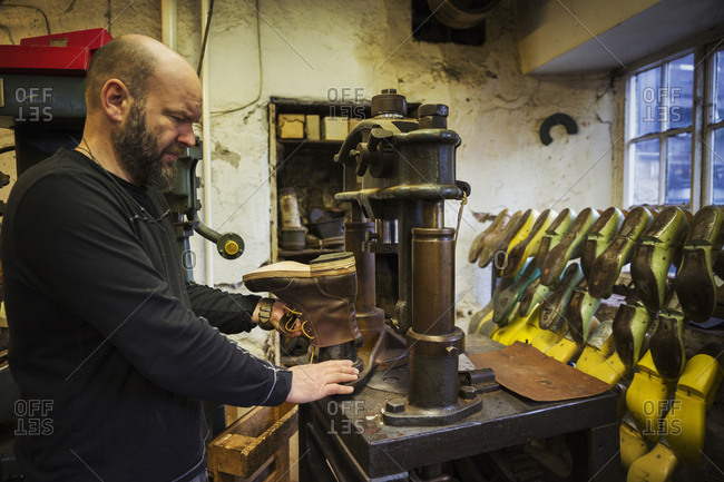 Man standing in a shoemaker's workshop, using a machine to make a leather ankle boot