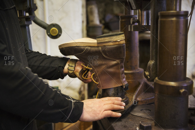 Close up of worker in a shoemaker's workshop, using a machine to make a leather ankle boot