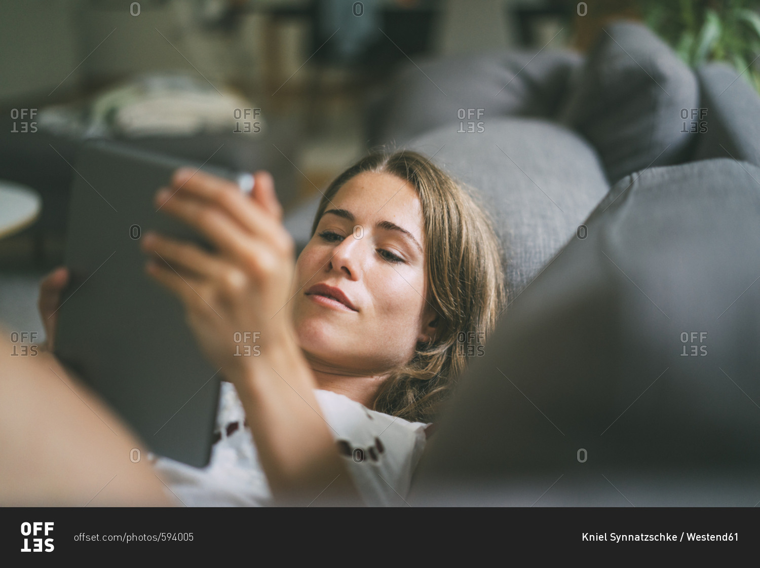 Relaxed young woman lying on couch using tablet