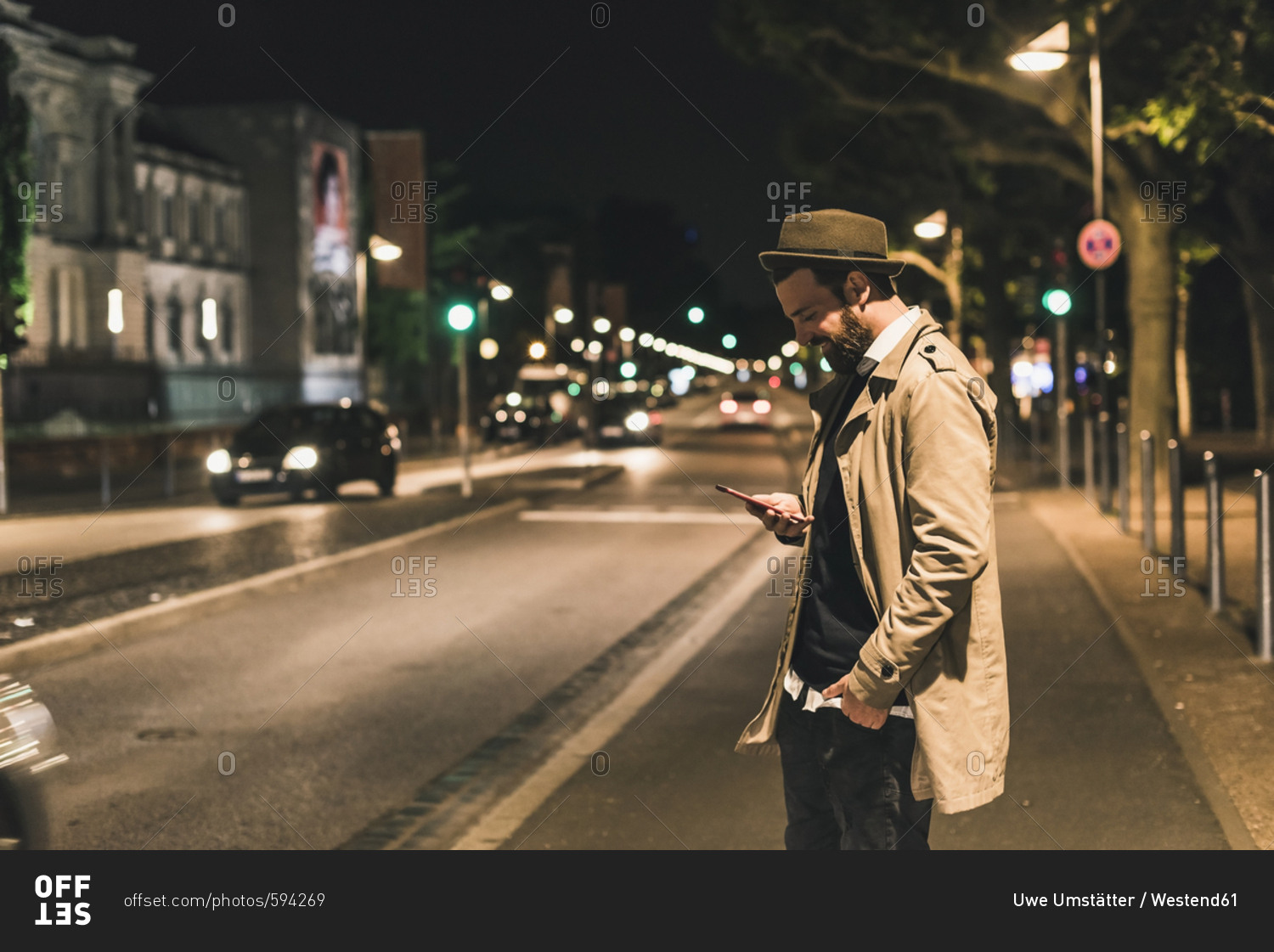 Stylish young man with cell phone on urban street at night