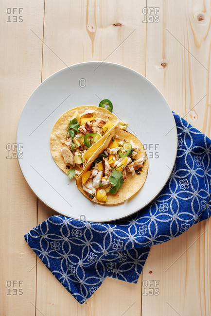 Gluten free fish tacos (Mahi Mahi) over corn tortillas, and mango salsa with jalapenos and cilantro on a single plate near a single blue linen.