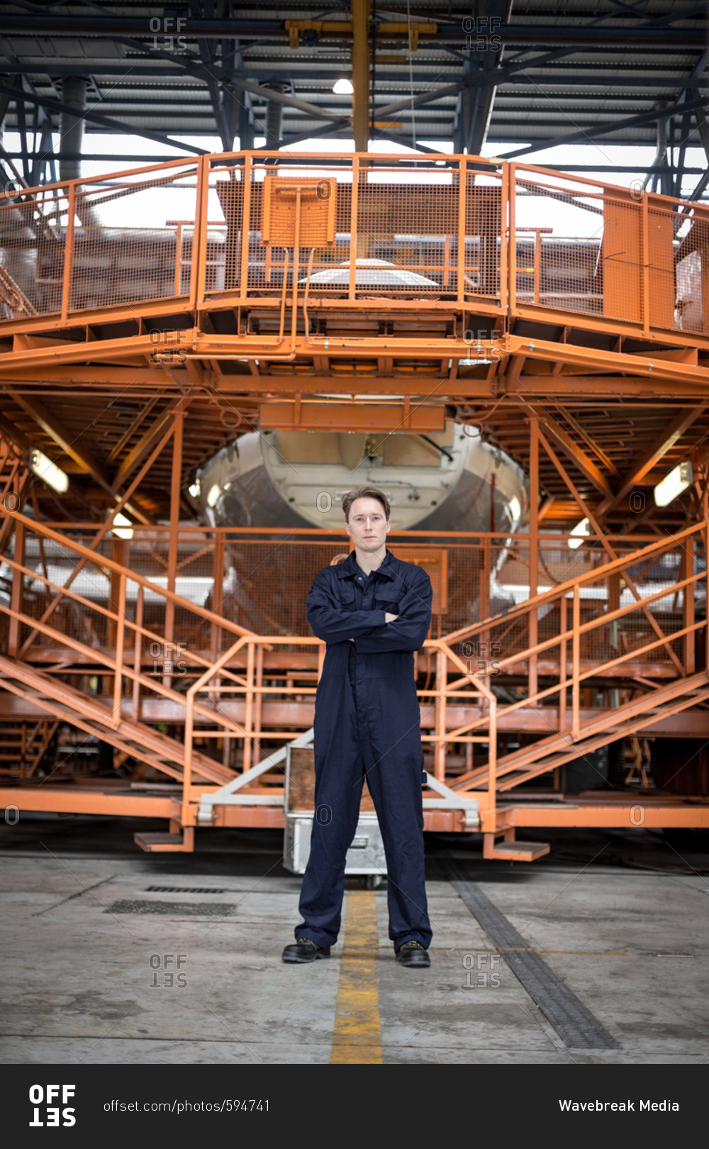 Portrait of female aircraft maintenance engineer standing with arms crossed at airlines maintenance facility