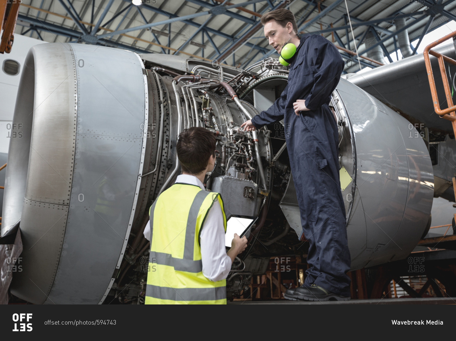 Male aircraft maintenance engineers examining turbine engine of aircraft at airlines maintenance facility