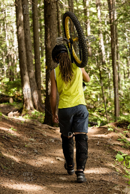 Rear view of woman carrying unicycle amidst trees