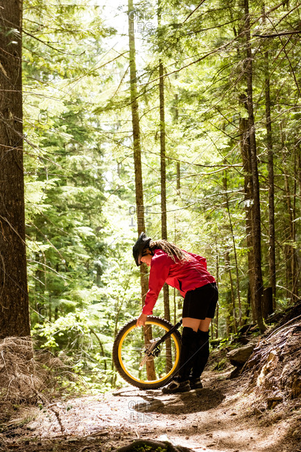 Woman adjusting unicycle while standing on trail against trees