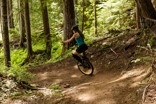 Rear view of woman unicycling on trial against trees in forest