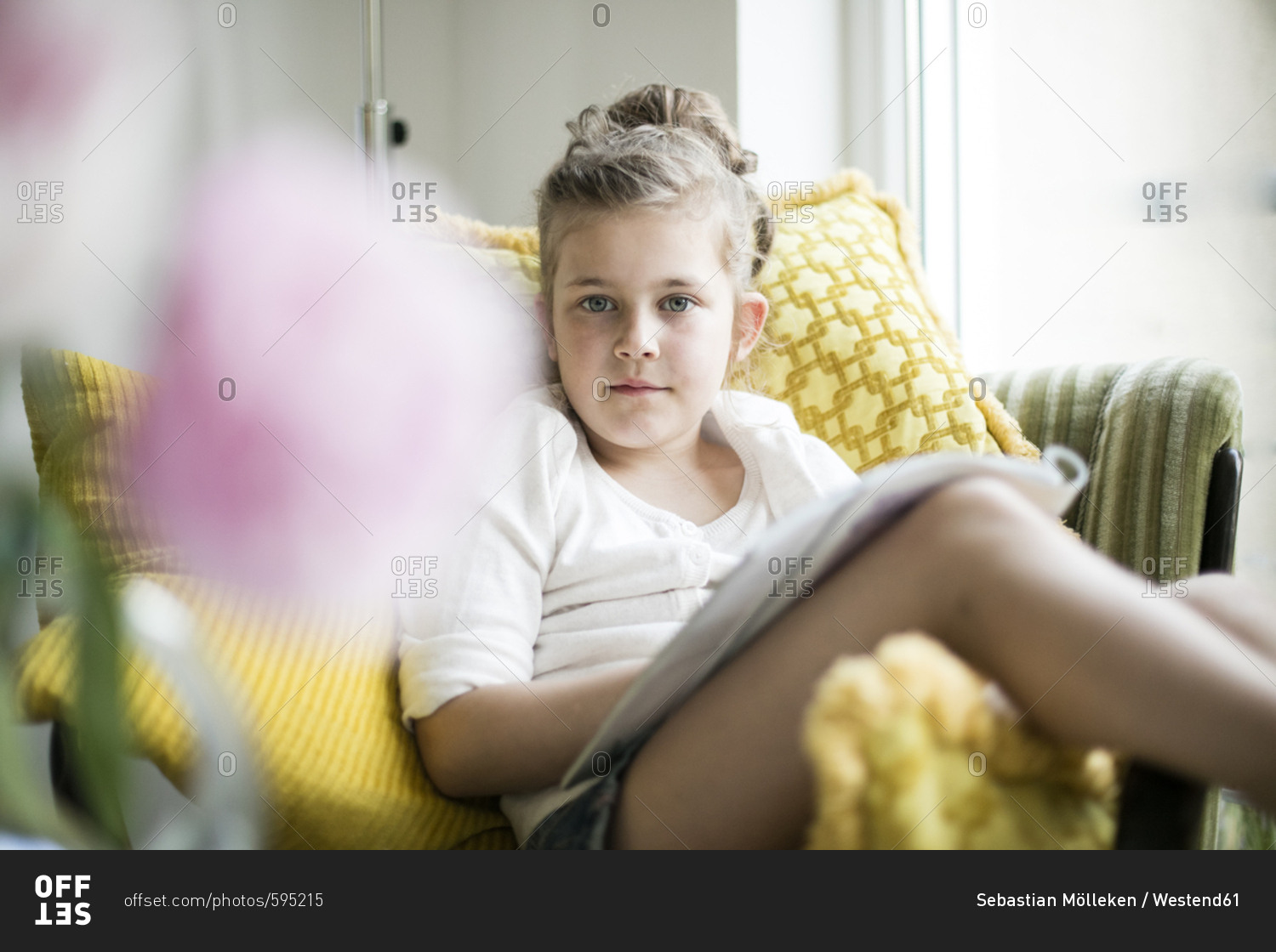 Portrait of relaxed little girl sitting with magazine on armchair