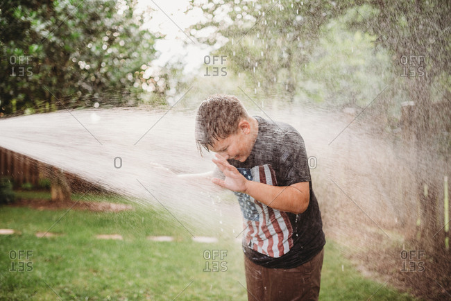 Boy in a backyard being sprayed with a water hose