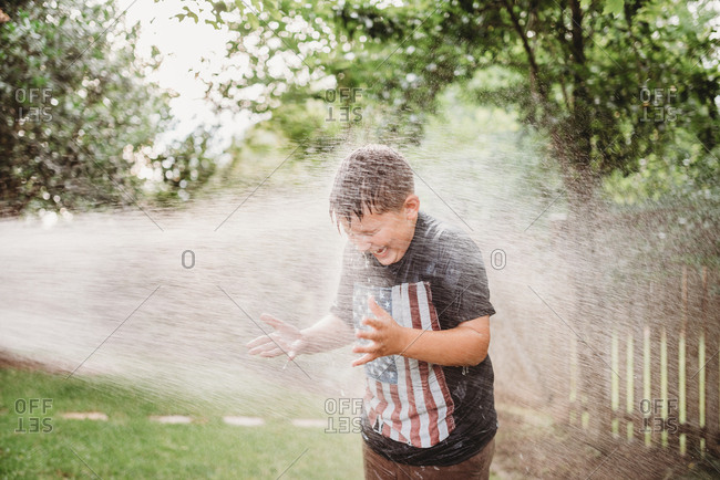 Boy being sprayed with a garden hose in a backyard