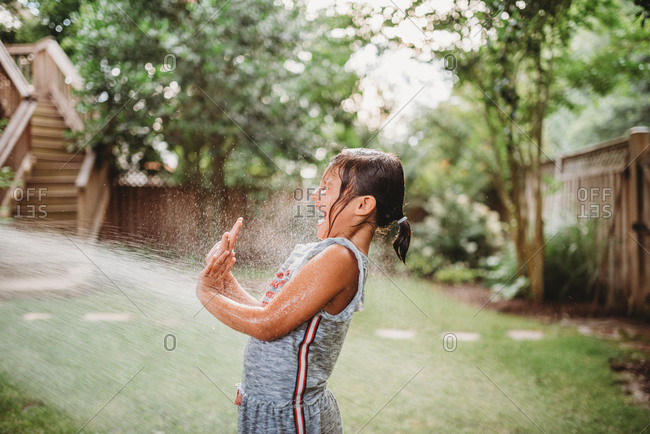 Little girl being sprayed with a water hose in a backyard