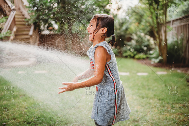 Little girl in a backyard being sprayed with a garden hose