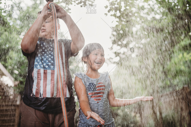 Sister and brother standing under spray from a garden hose