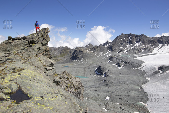 A hiker standing on a rocky peak near the Rosa Blanche. He is looking over a barren landscape, created when the glaciers retreated. This is halfway the Haute Route, a classic trekking in Europe.