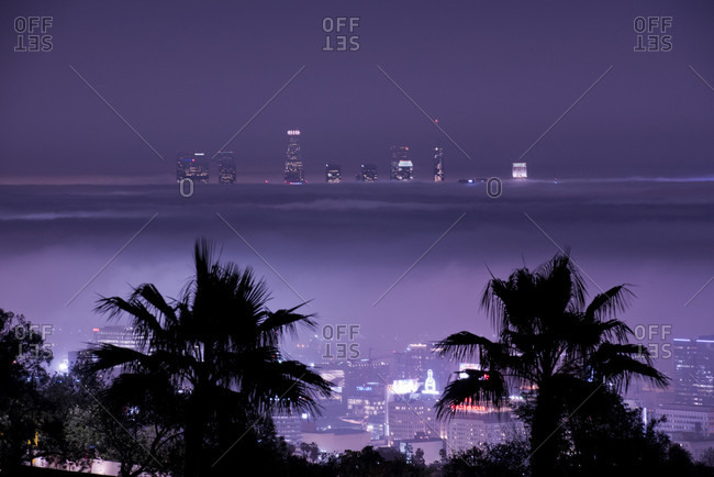 The Los Angeles skyline sticks out through a layer of fog at night.
