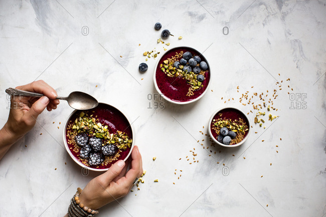 Person holding a smoothie bowl topped with pistachios and frozen berries