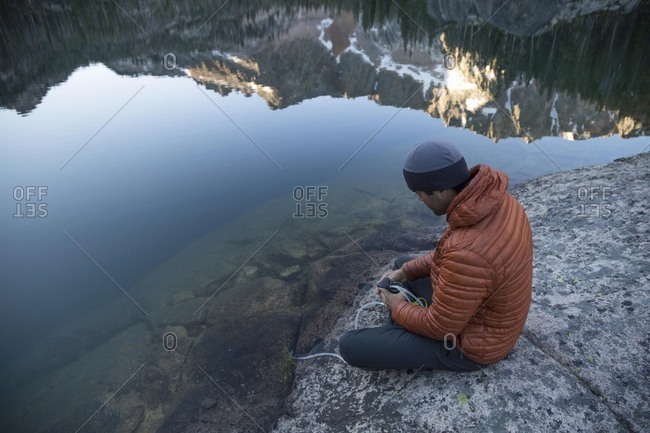 High angle view of man filling water bottle from lake while sitting on rock