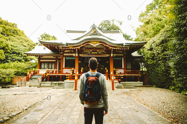 Back view of man with backpack standing at the Asian style temple. Horizontal outdoors shot.