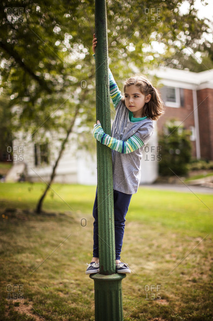 A young girl climbing a streetlight pole in a park