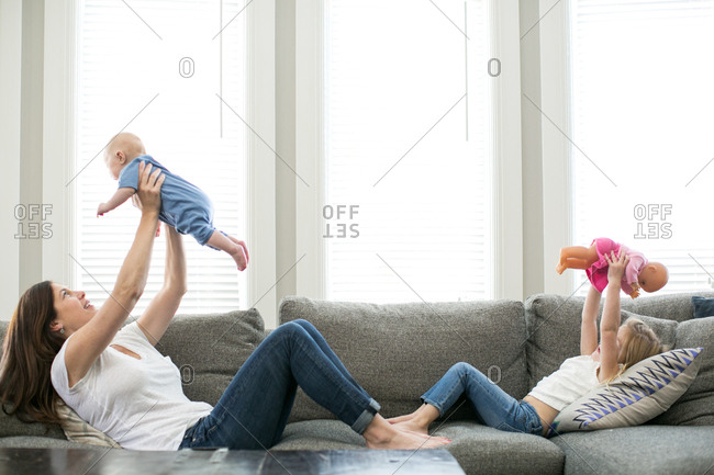 Mother holding baby boy in air across from daughter holding doll in air