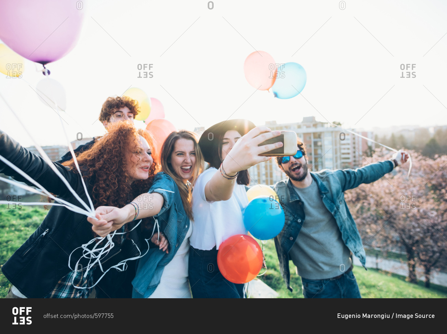 Group of friends enjoying roof party, holding helium balloons, young woman taking selfie using smartphone