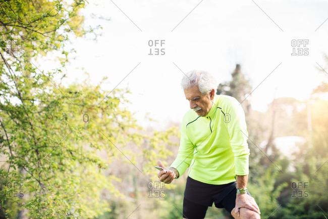 Senior man hand on knee looking at smartphone