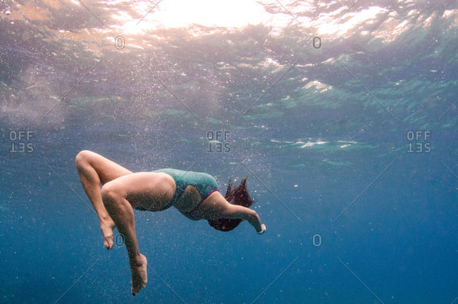 A woman in a green bathing suit does a back flip under water