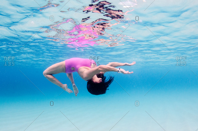 A woman in a pink bathing suit does a back flip in clear blue water