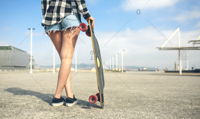 Back view of young woman with longboard in front of beach promenade- partial view